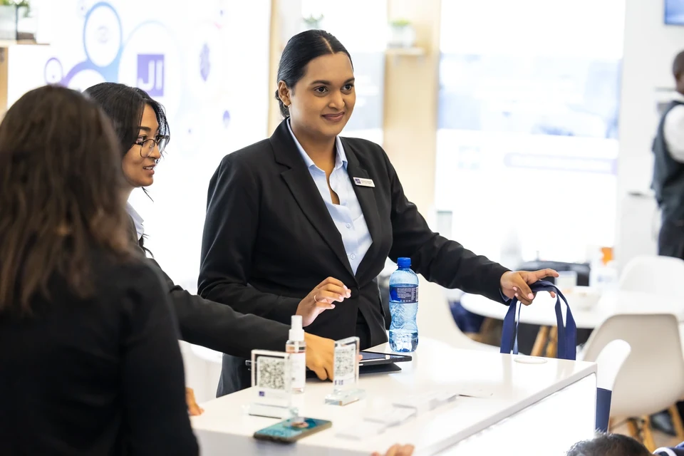 Staff and visitors at the exhibition counter with branded bags and QR code displays.