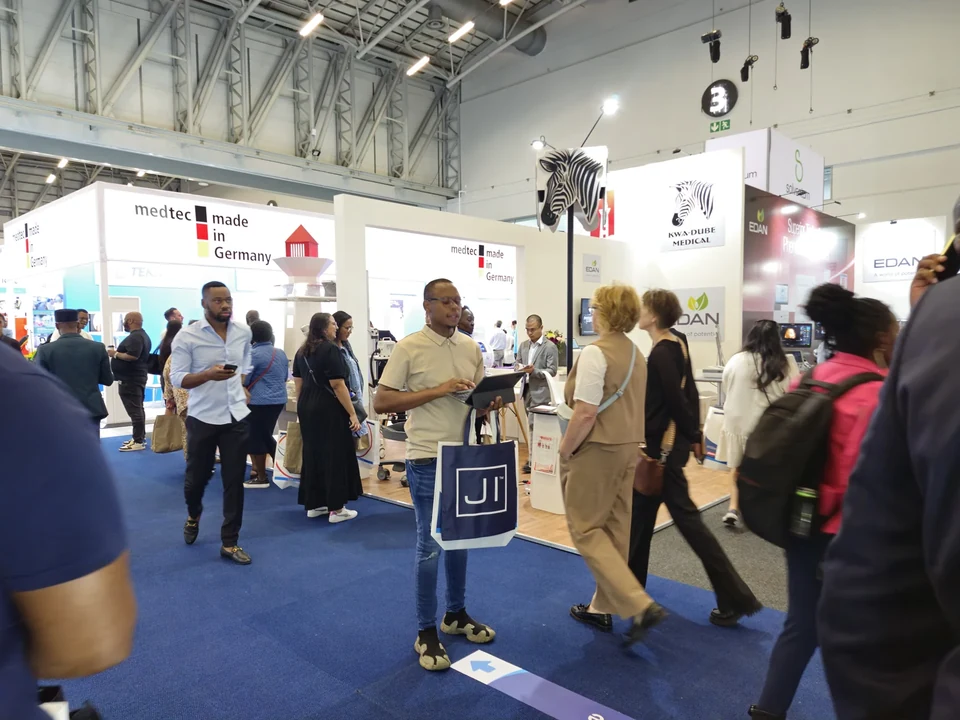 A visitor carrying a navy Jehu Industries tote bag through an Africa Health exhibition aisle.