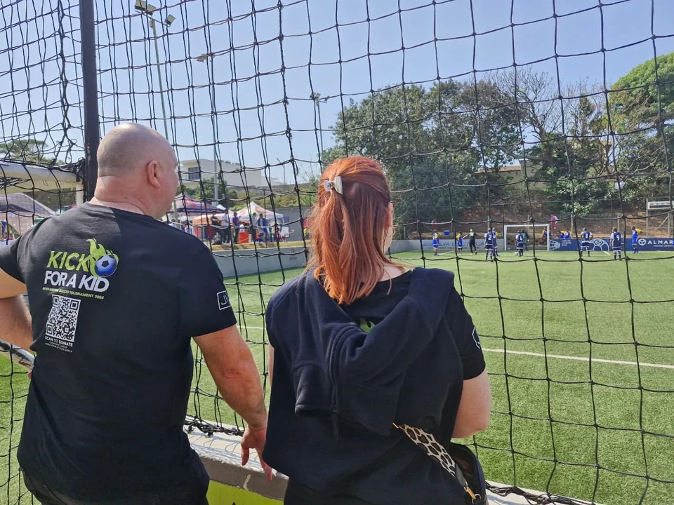Spectators wearing the Kick for a Kid event identity beside the football pitch.